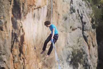 A man is walking along a stretched sling. Highline in the mountains. Man catches balance. Performance of a tightrope walker in nature. Highliner on the background of the mountains.
