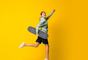 Fototapeta na wymiar Blonde teenager skater girl jumping over isolated yellow background