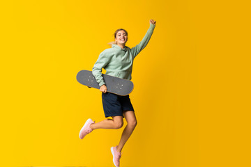 Blonde teenager skater girl jumping over isolated yellow background © luismolinero