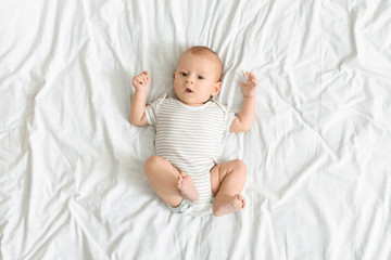 Curious baby lying on bed and looking to camera