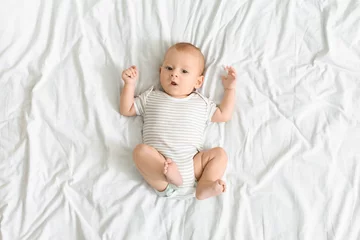 Fototapeten Curious baby lying on bed and looking to camera © Prostock-studio