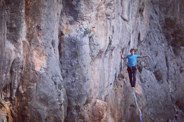 A man is walking along a stretched sling. Highline in the mountains. Man catches balance....