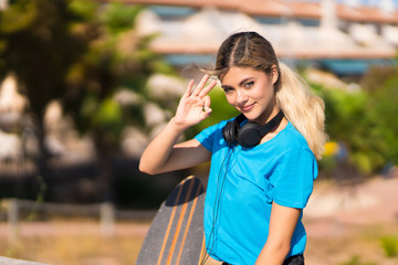 Teenager girl with skate at outdoors showing ok sign with fingers