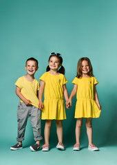 Fototapeta premium portrait of children on a light background: full body shot of three children in bright clothes, two girls and one boy. Triplets, brother and sisters.