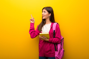 Teenager student girl on vibrant yellow background pointing with the index finger a great idea