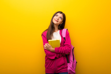 Teenager student girl on vibrant yellow background looking up