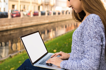 Female smart university student online learning via laptop computer with empty mock up copy space screen background for promotional content, sitting outdoors near waterfront