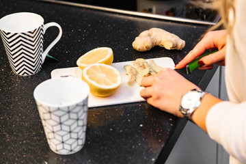 Woman's hand slicing lemon for tea on dark table
