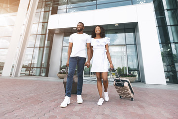 Happy black couple going with luggage out of airport building