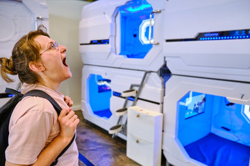 Obraz premium A young woman yawns and wants to sleep next to the rooms of a mini hotel. Capsule hotel - one of the variants of high tech hotels, which is a small sleeping cells located on top of each other