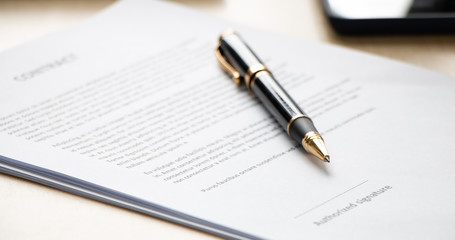 Close up of ball pen lying on a contract paper or application form on office desk, low angle view and selected focus. Signing the business contract concept.