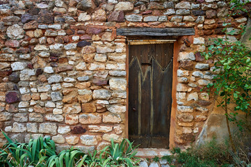 Fototapeta na wymiar Ancient wooden door in a red ochre stone wall