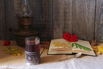 The still life of glass of tea, vintage lamp and autumn foliage on the grey wooden background.