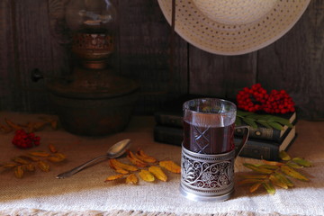 The still life of glass of tea, vintage lamp and autumn foliage on the grey wooden background.
