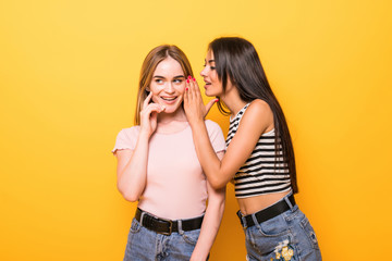 Portrait of two beautiful gossiping girls against orange background