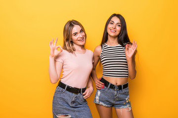 Close-up portrait of two girls wearing casual showing ok-sign isolated over orange background