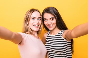 Two cheery young teenage girls taking a selfie while standing against orange wall