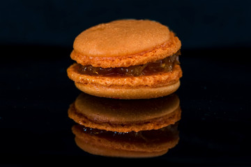 One orange macaroon on a black background, close up, macro photography
