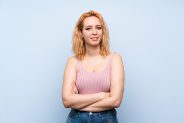 Young woman over isolated blue background keeping the arms crossed in frontal position