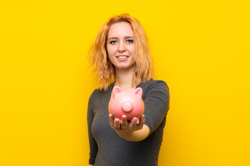 Obraz na płótnie Canvas Young woman over isolated yellow background holding a big piggybank