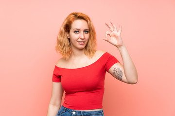 Young woman over isolated pink background showing ok sign with fingers