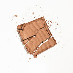 A makeup product, cracked in pieces on a white background