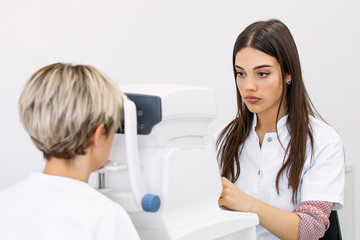 Pleasant woman with blue eyes having her eyes checked in binocular apparatus the oculist in eyes...