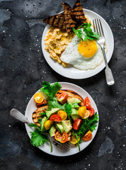 Savory breakfast - avocado, cherry tomatoes grilled  bread salad and fried egg with hummus and rye croutons on dark background, top view