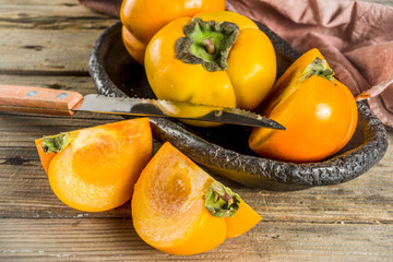 Whole and sliced persimmons, fresh organic farm fruit on rustic wooden background. Isolated, copy space
