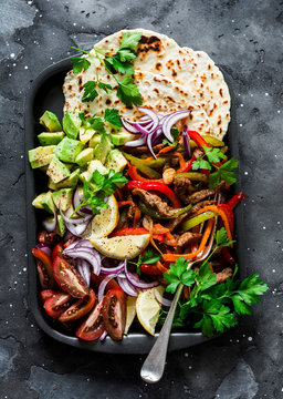 Spicy beef, vegetables, avocado, corn tortillas fajitas on a sheet pan on a dark background, top view. Delicious snack, tapas in mexican style