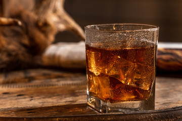 Glass of Whisky (whiskey), bourbon, ice tea or coke (cola) soda with ice and water drops on wood table and newspaper at dark background with copy space, close up