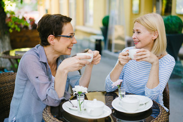 Attractive ladies happy friends are chatting in outdoor cafe holding coffee cups smiling relaxing...