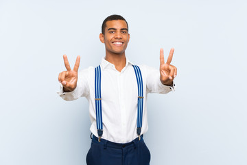 Young handsome brunette man with suspenders over isolated background smiling and showing victory sign