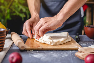 Man chef in a black apron kneads the dough with hands for Christmas baking. Joyful cooking for festive new year table
