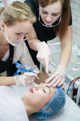 Decorative cosmetology courses. Beautician teaching female intern how to use tattoo machine for...