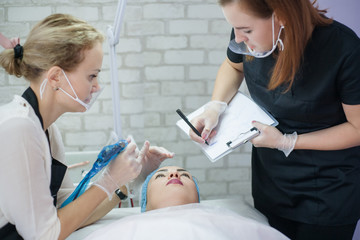 Permanent makeup class. Beautician teaching female intern how to sketch up symmetrical eyebrows.