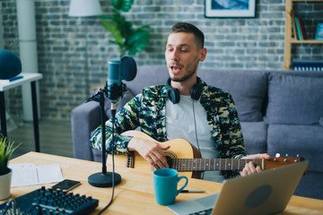 Blogger handsome young man is playing the guitar and singing recording music in modern studio using...