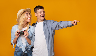 Young tourists holding camera and pointing away over yellow background