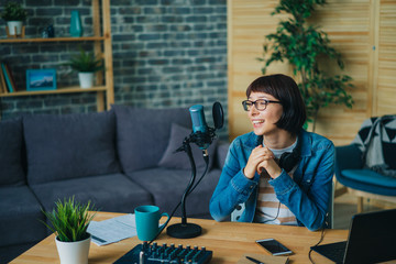Happy girl blogger is speaking in microphone in recording studio smiling creating podcast for...