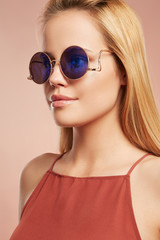 Close-up portrait shot of a young blonde European lady with straight long hair dressed in a ruddy top with thin shoulder-straps. The girl is wearing stylish circle sunglasses with lustrous rim,  © RedUmbrella&Donkey