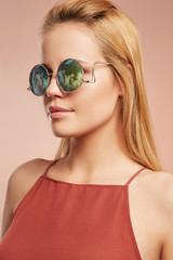 Close-up portrait shot of a young blonde European lady with straight long hair dressed in a ruddy top with thin shoulder-straps. The girl is wearing stylish circle sunglasses with lustrous rim,  © RedUmbrella&Donkey