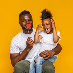 Cheerful afro daddy and his little daughter posing with photo props