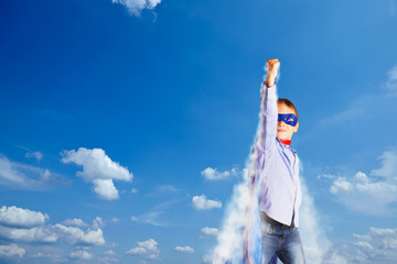 Young boy is playing like a superhero in front of a blue sky background.