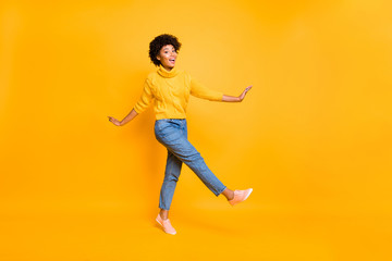 Fototapeta na wymiar Full length body size photo of cheerful black afro american woman dancing or moving forward wearing jeans denim yellow pullover sneakers isolated with vivid color yellow background
