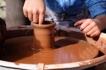 The potter teaches the child how to form a clay jug on a potter's wheel.