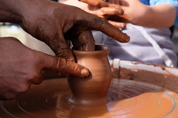 The potter teaches the child how to form a clay jug on a potter's wheel.