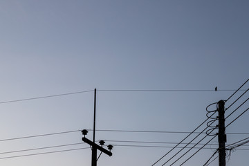 Silhouette of an electric pole and a bird facing the right, perched on an electric wire