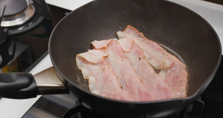 Cooking bacon on the fry pan in kitchen for breakfast