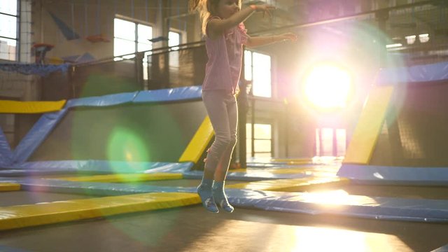 Little kid girl has fun playfully jumping and rolling in trampoline amusement park playground