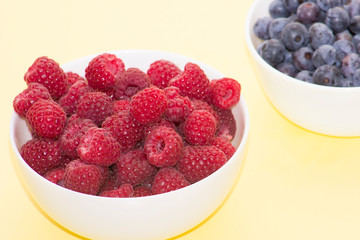 Forest berries, raspberries, blueberries in a bowl on a yellow background from above
